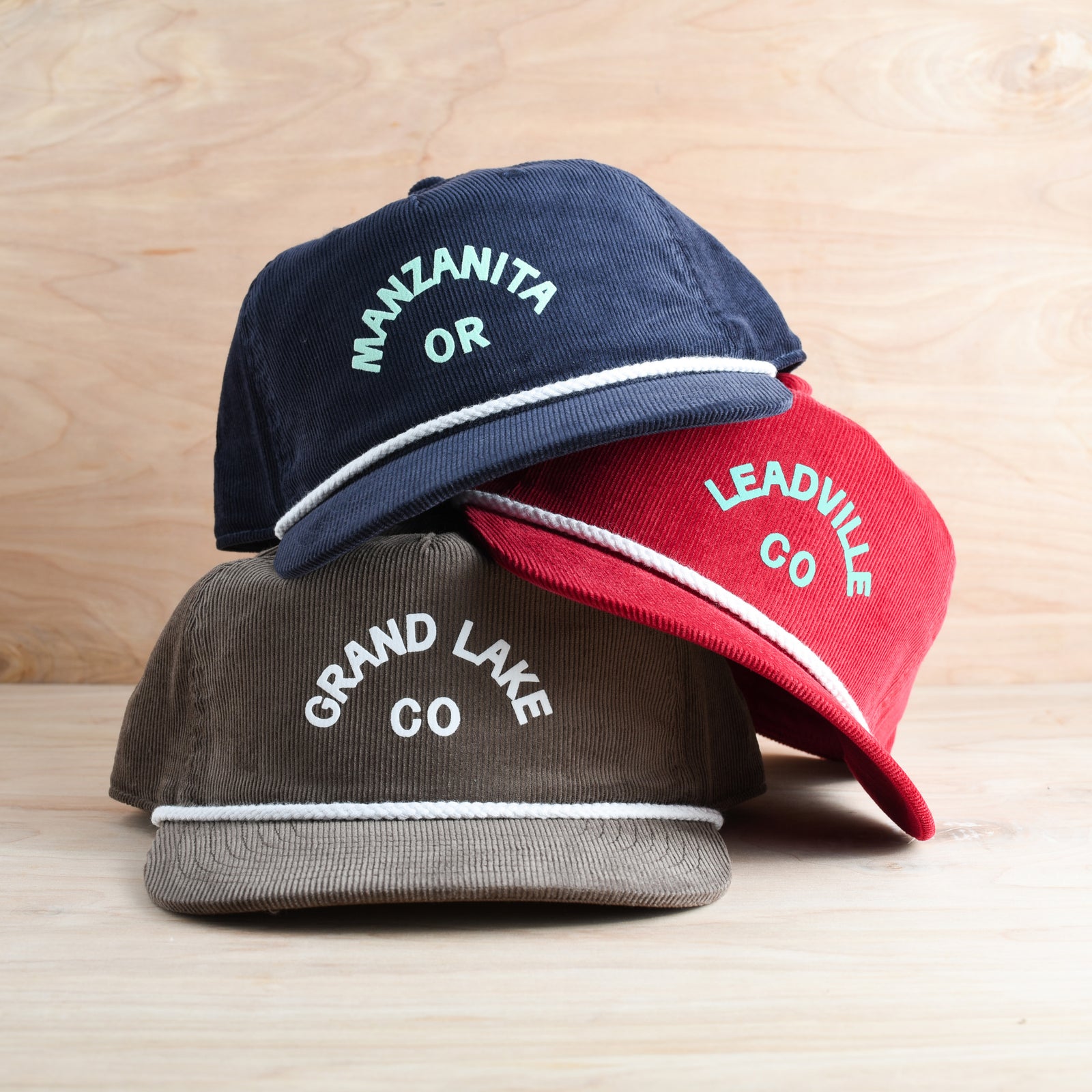 Three customizable corduroy snapback hats with city and state on front on a wooden background.